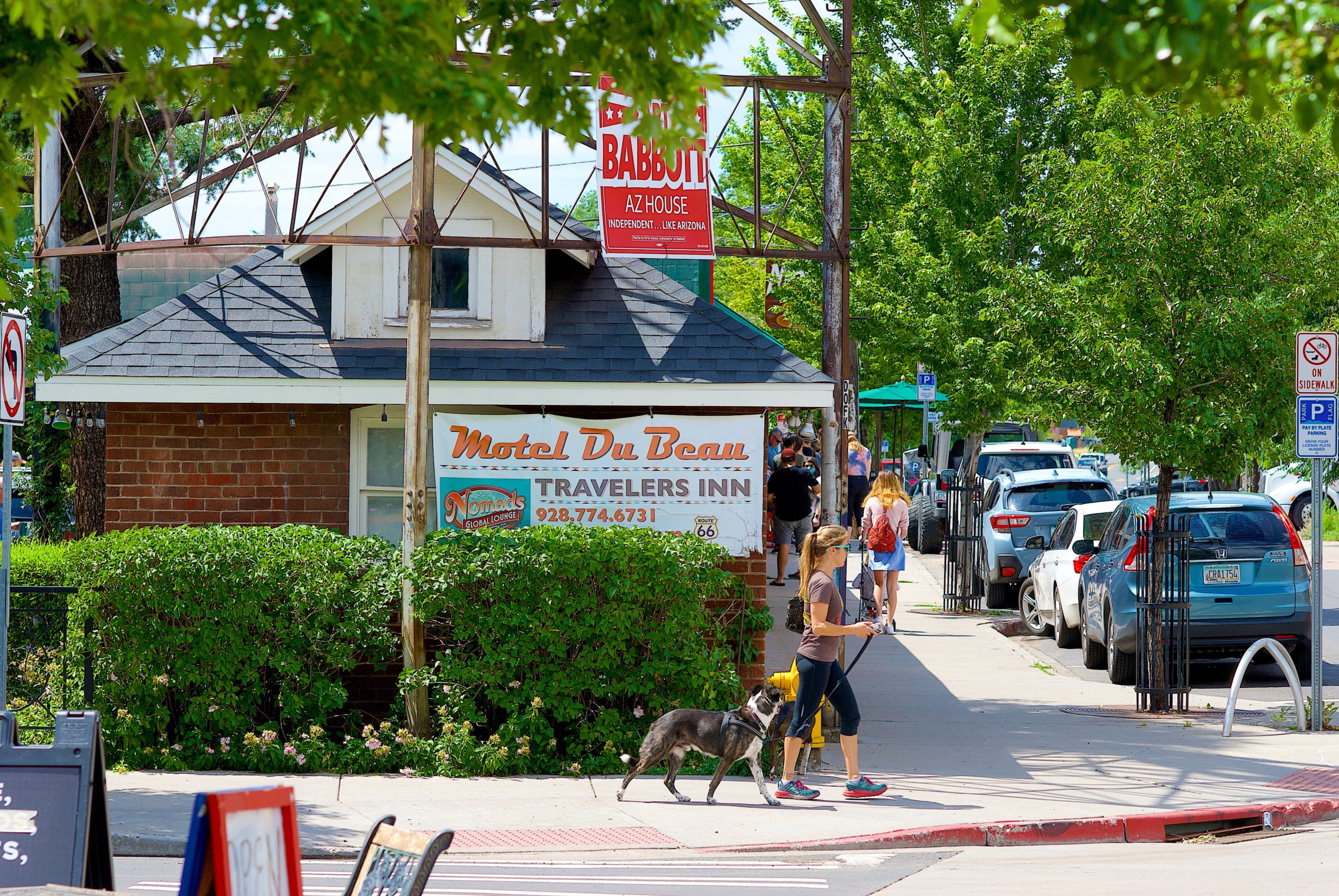 Flagstaff, Arizona / USA - July 25, 2020: A woman walks her dog past the historic Route 66 Motel Du Beau as masked and unmasked customers wait in line for lunch in the background on a sunny summer afternoon in the heart of Flagstaff’s historic district.