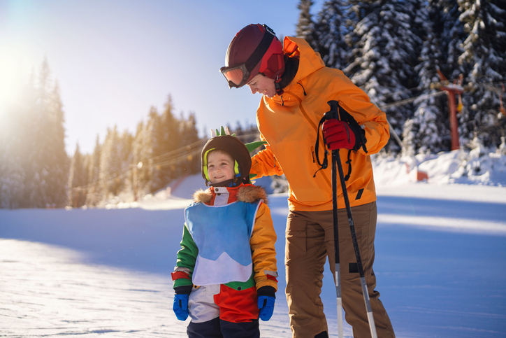 Mother teaches her son to ski while enjoying a sunny day on a snowy slope. The family connection is evident as they share an outdoor adventure amidst a picturesque alpine setting.